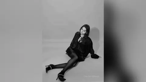 Elegant woman in a chic black outfit sitting on a studio floor in a moody black and white portrait.