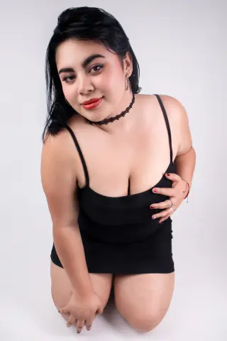 Smiling young woman in a black tank top posing against a white background for a minimalist portrait.