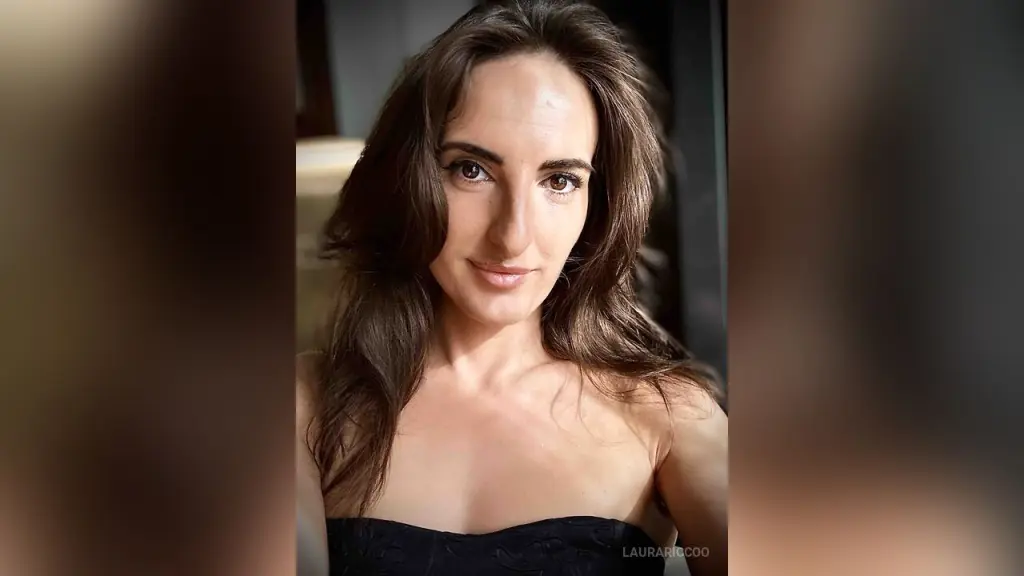 LauraRiccoo sits on a chair wearing a black silk slip dress while holding a smartphone.