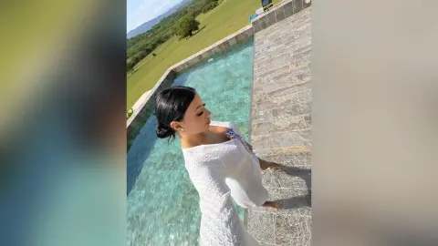 Aleja poses in a white knit dress next to a clear blue swimming pool.