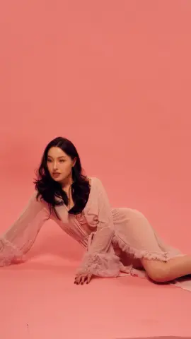Elegant woman in a sheer pink ruffled dress sitting against a soft pink background with a dreamy mood.