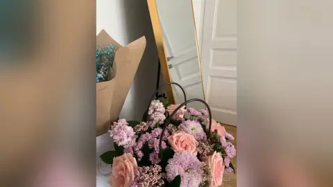 SabrinaSteels displays a large bouquet of pink roses and light purple flowers next to a wrapped bunch of blue flowers and a gold-rimmed mirror.
