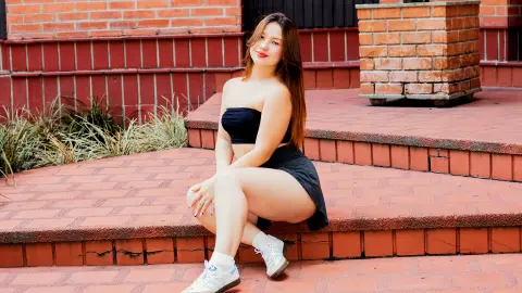 Young woman in a black strapless top and skirt sitting on brick steps in a relaxed outdoor setting.