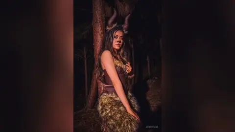 JessieLiu poses in a forest wearing a brown furry animal costume with horns and a dark bra.