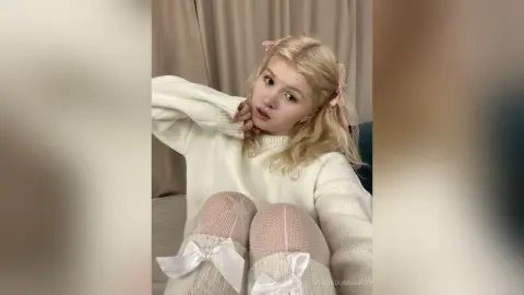 Blonde woman in a cozy white sweater and sheer patterned tights posing in a soft, dreamy indoor setting.