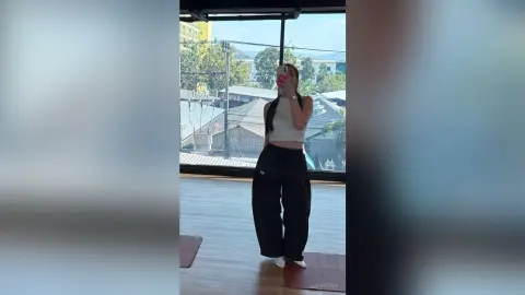 LiaMotzer stands in a white crop top and black trousers in front of a large window overlooking a city view.