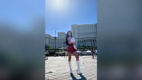 Young woman in a white crop top and red mini skirt posing in a sunny city plaza near grand architecture.