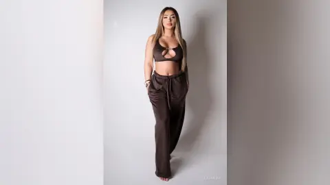 Young woman in a brown cutout crop top and matching wide-leg lounge pants posing in a bright studio.
