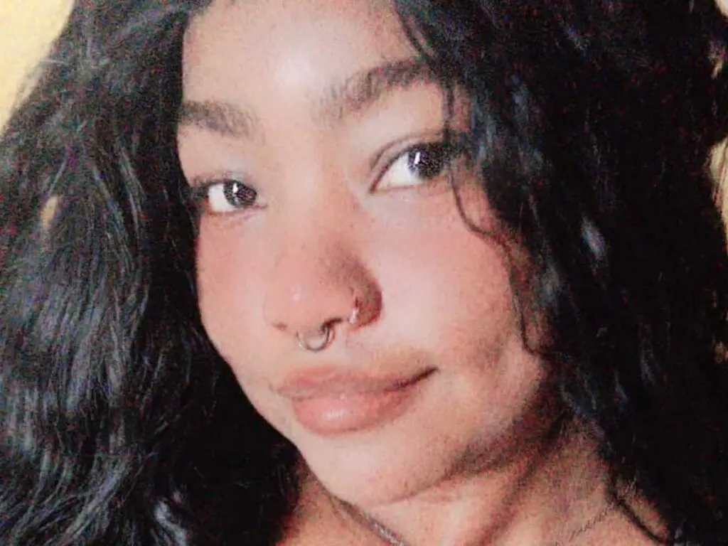 Close-up portrait of a smiling woman with curly dark hair and a nose ring in soft natural lighting.