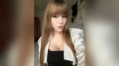 SharikaGlidden poses in a white jacket and black top, showing off her long brown hair and cleavage.