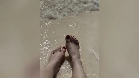 Close-up of bare feet resting on wet sandy beach with gentle ocean waves in a relaxing summer mood.