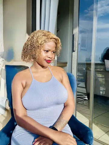 Smiling woman in a light blue ribbed sundress sitting on a sunny balcony.