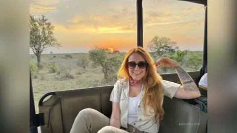 Smiling woman in a white linen shirt and sunglasses enjoying a sunset safari ride in the African savanna.