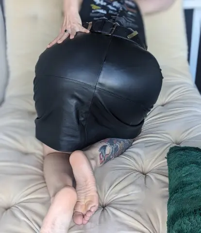 Woman in a black leather skirt sitting on a beige tufted sofa in a relaxed mood.