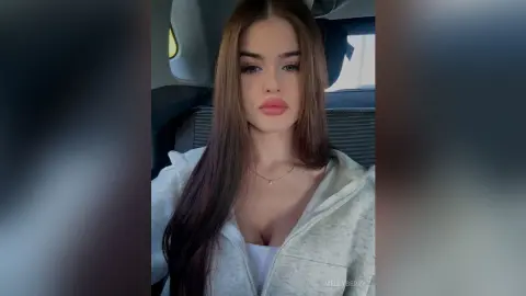 Young woman with long brown hair wearing a white hoodie sitting in a car with a soft, natural look.
