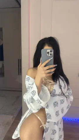 Young woman in a white patterned lace robe taking a mirror selfie in a modern bedroom.