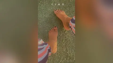 Top-down view of a person's bare feet on green grass wearing striped lounge pants in a relaxed summer mood.