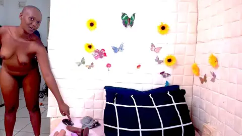 Nude Black woman in a bright bathroom with butterfly wall decor and a navy plaid pillow.