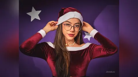 JessieLiu wears a red velvet Santa hat and a matching off-the-shoulder velvet top while posing against a purple background.