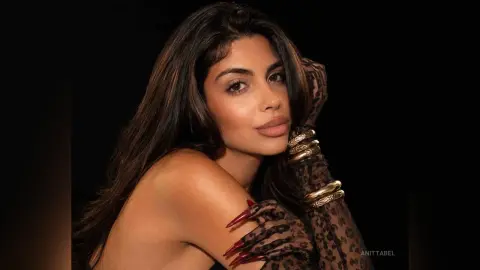 Glamorous woman in leopard print gloves and gold jewelry posing against a dark background.