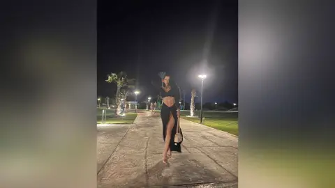 NicoleBella stands on a paved path at night wearing a black cut-out bodysuit with a high slit.