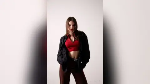 Confident woman in a red crop top and black jacket posing against a minimalist white studio background.