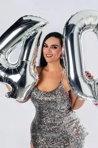 Smiling woman in a sparkly silver sequin dress holding large silver number 40 balloons for a birthday celebration.