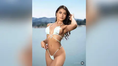 Beautiful woman in a white string bikini posing on a sunny beach with ocean background.