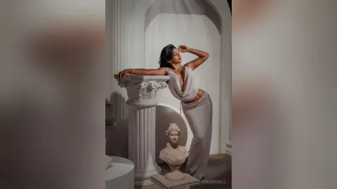 Elegant woman in a white silk gown posing gracefully by classical marble columns in a dreamy, ethereal setting.