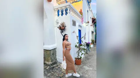 CristalMatthews stands outdoors against a white wall wearing a tan cutout dress and white sneakers.