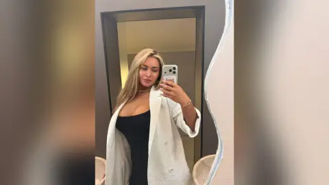 SelenaRusse takes a mirror selfie wearing a black top and an open white blazer.
