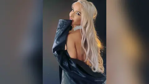 Glamorous blonde woman in a black leather jacket and diamond choker posing against a dark studio background.