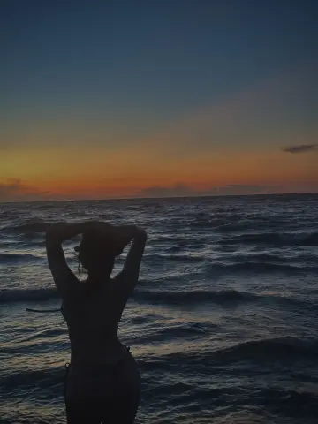 Silhouette of a woman in a bikini enjoying a peaceful sunset over the ocean waves at the beach.