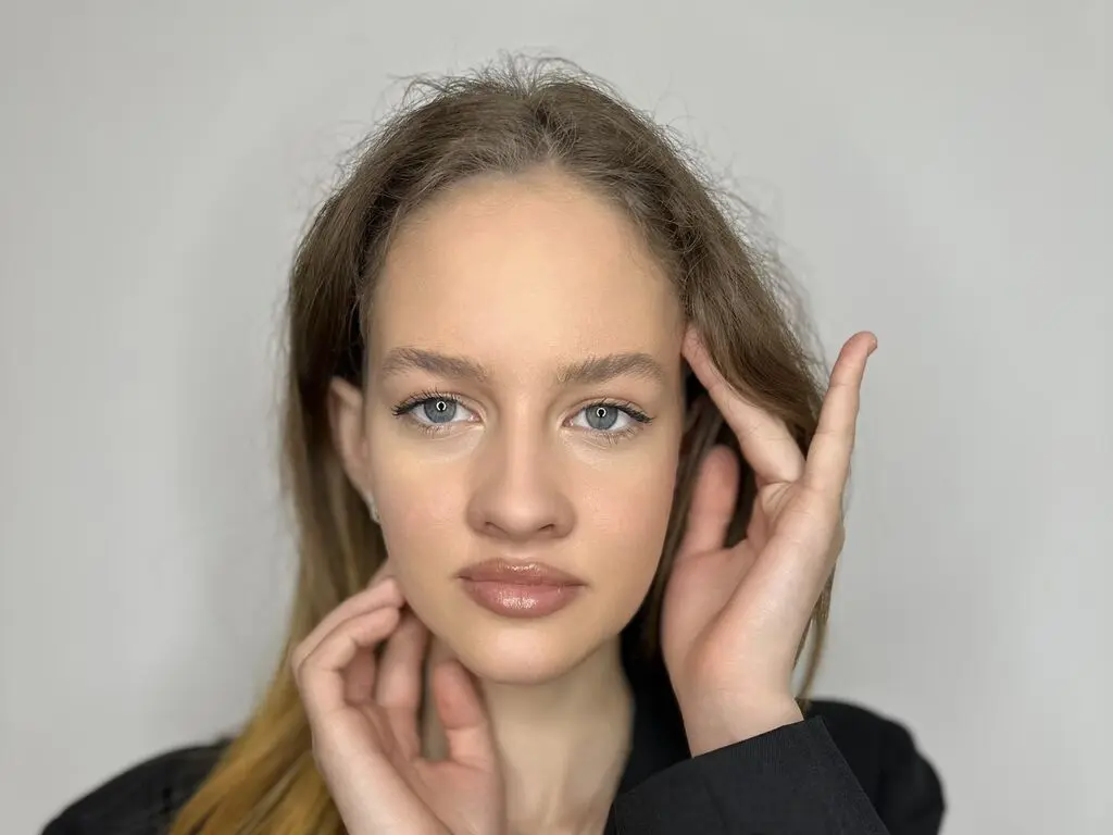 Young woman with long brown hair and natural makeup posing against a plain white background.