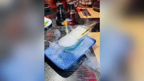 Refreshing blue smoky cocktail served on a blue patterned tray in a moody restaurant setting.