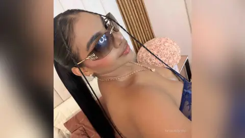 Stylish woman in dark sunglasses and blue outfit relaxing in a bright, modern room.