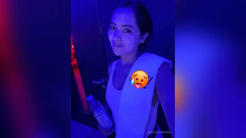 Smiling woman in a white tank top holding a water bottle in moody blue lighting.
