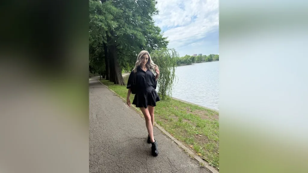 Maddy — MaddyScarlett stands on a paved path next to a lake wearing a short black dress.