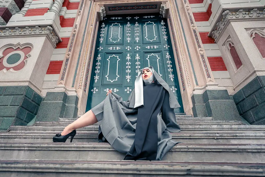 NikolleWilliams — Nun in a black and grey habit sitting on stone stairs in front of an ornate teal cathedral door.