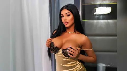 Glamorous woman in a gold satin dress posing with long dark hair in a modern indoor setting.