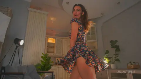 Cheerful woman in a floral summer dress twirling in a bright, modern living room.