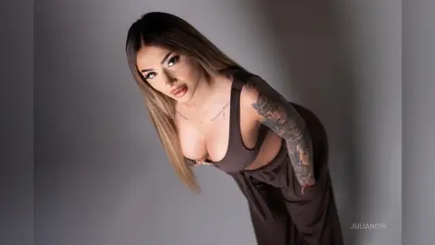 Glamorous woman in a brown crop top and trousers posing with a confident expression against a grey studio backdrop.