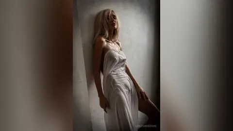 LeslyAnderson poses against a wall wearing a white strapless slip dress that drapes over her body.