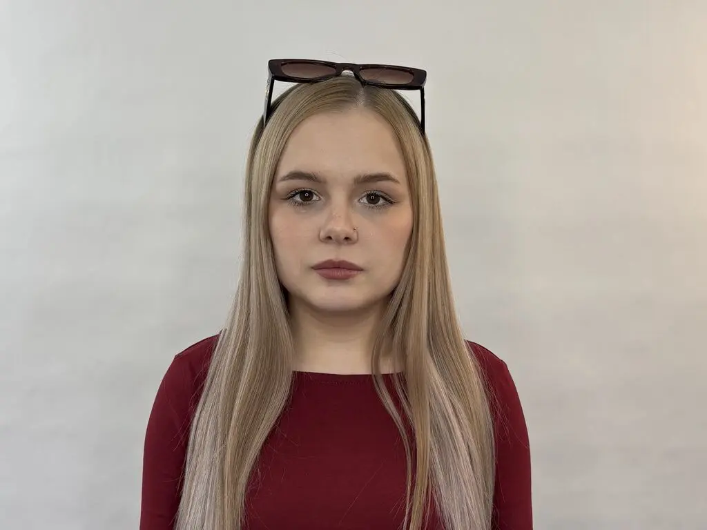 Blonde woman in a burgundy top with sunglasses on her head against a plain white background.