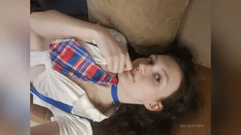 Young woman in a white blouse and blue patterned tie relaxing on a brown couch in a cozy indoor setting.