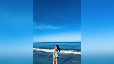 Young woman in a mint green bikini relaxing on a sunny beach under a clear blue sky.