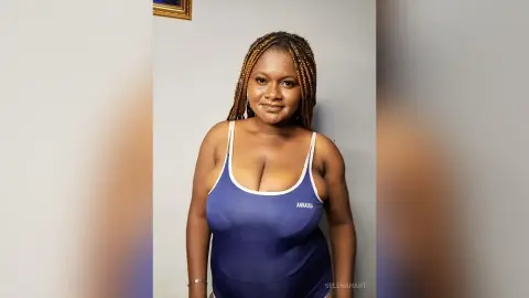 Smiling Black woman with braided hair wearing a blue bodysuit in a bright indoor setting.
