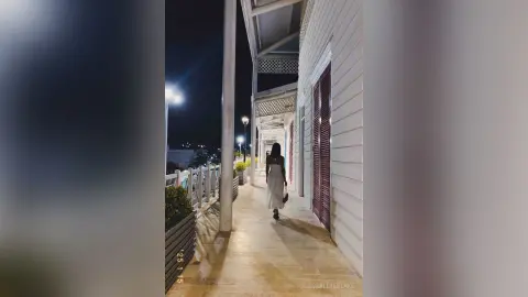 Elegant woman in a white dress walking along a moonlit balcony at a luxury resort at night.