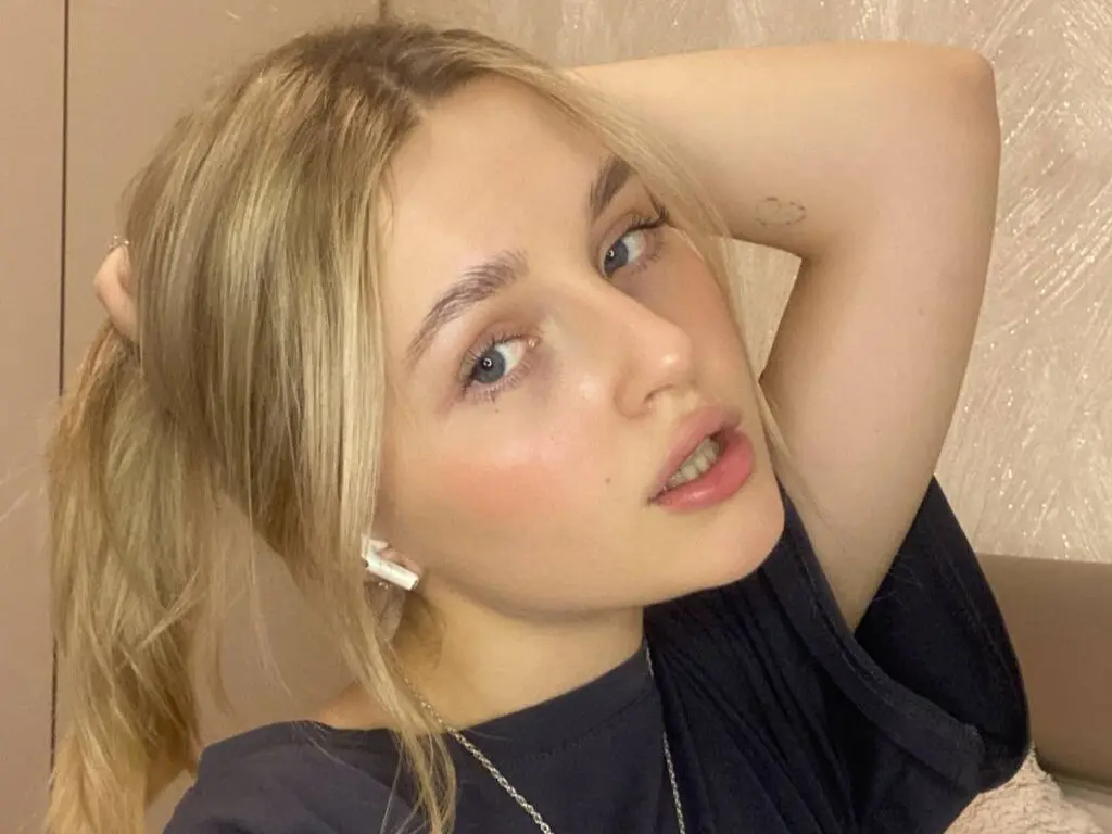 Blonde woman in a black t-shirt posing with a relaxed expression in a bright indoor setting.