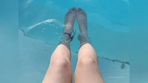 Close-up of legs relaxing in a clear blue swimming pool on a sunny summer day.